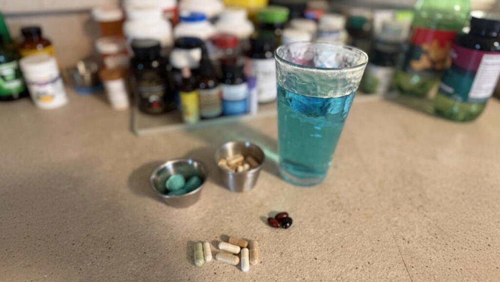 Supplements on kitchen counter with many more bottles of supplements in the background.