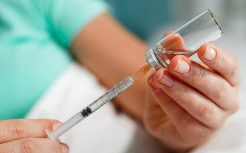 A woman's hand holding a research peptide vial while her other hand is drawing down the clear liquid into an insulin syringe, representing retatrutide