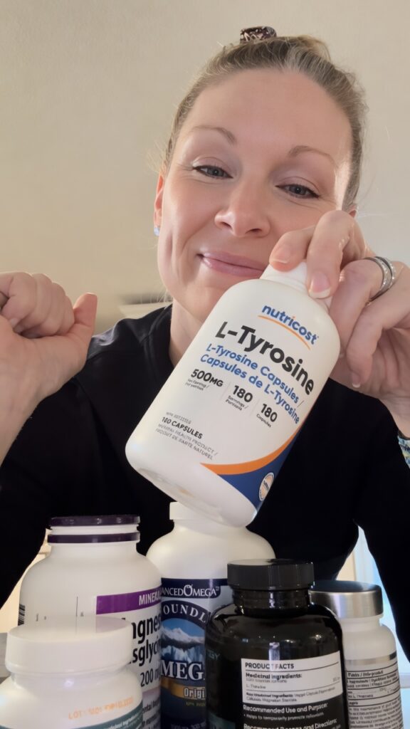 Smiling woman holding up a bottle of Nutricost L-Tyrosine 500mg capsules, with other wellness supplements arranged in the foreground. Perfect for supporting focus and motivation in an adult ADHD natural supplement routine