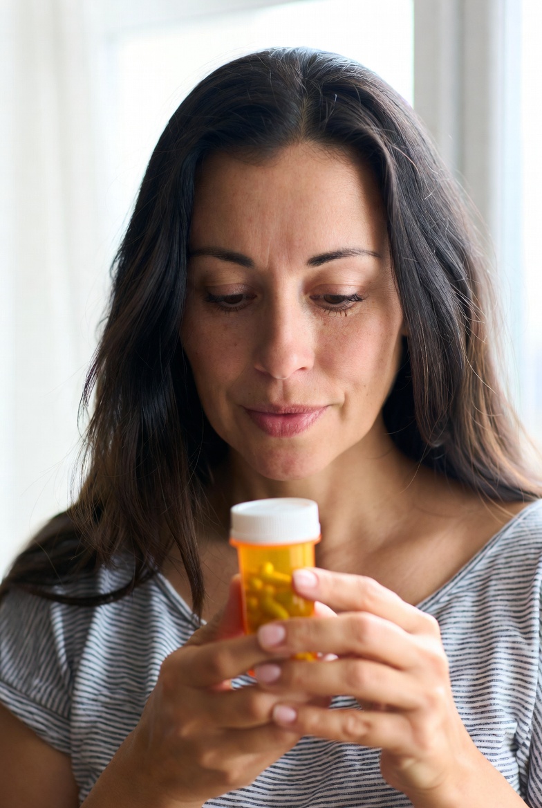 A woman in her late 30s thoughtfully examining a prescription pill bottle in warm golden hour light, capturing the frustration many experience with ADHD medication variability.