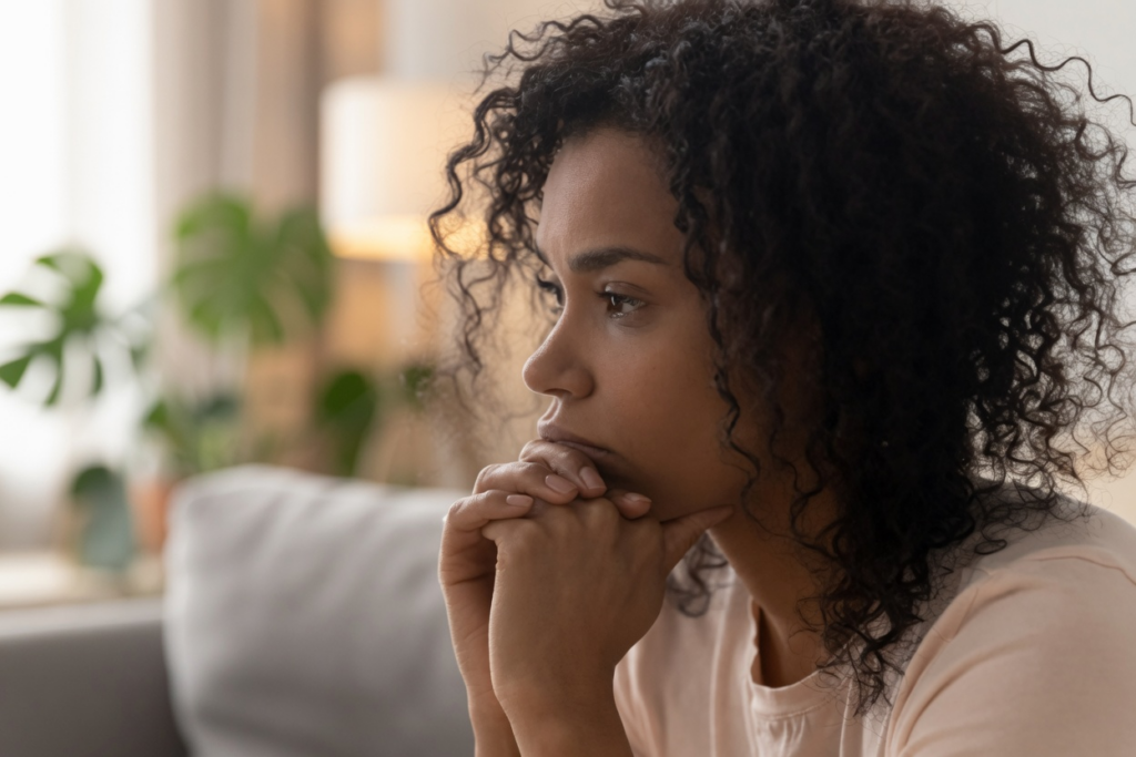 Woman with curly dark hair resting her chin on her hands, looking thoughtfully to the side in a softly lit living room, feeling grief after vyvanse stopped working