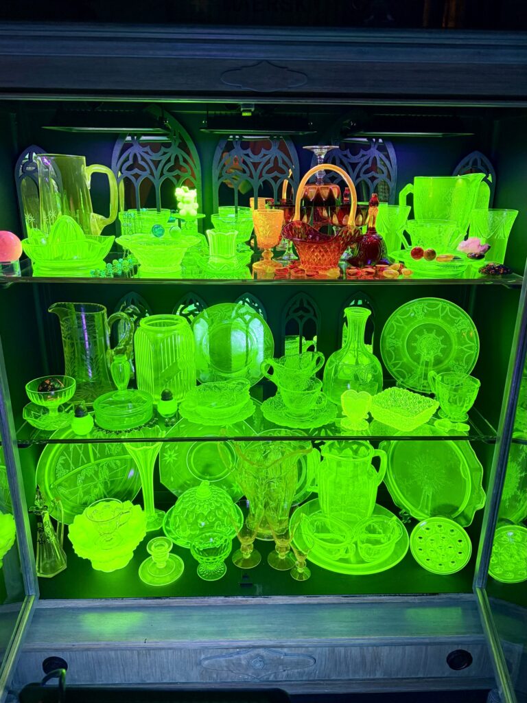 Uranium glass collection glowing under black lights in a cabinet, built by someone with an ADHD hyperfixation