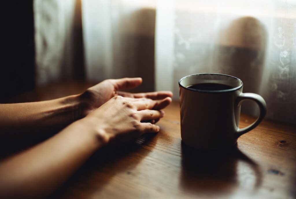 Soft morning light on a woman’s hands resting near a coffee mug, a quiet moment of pause in the RSD people pleasing ADHD cycle